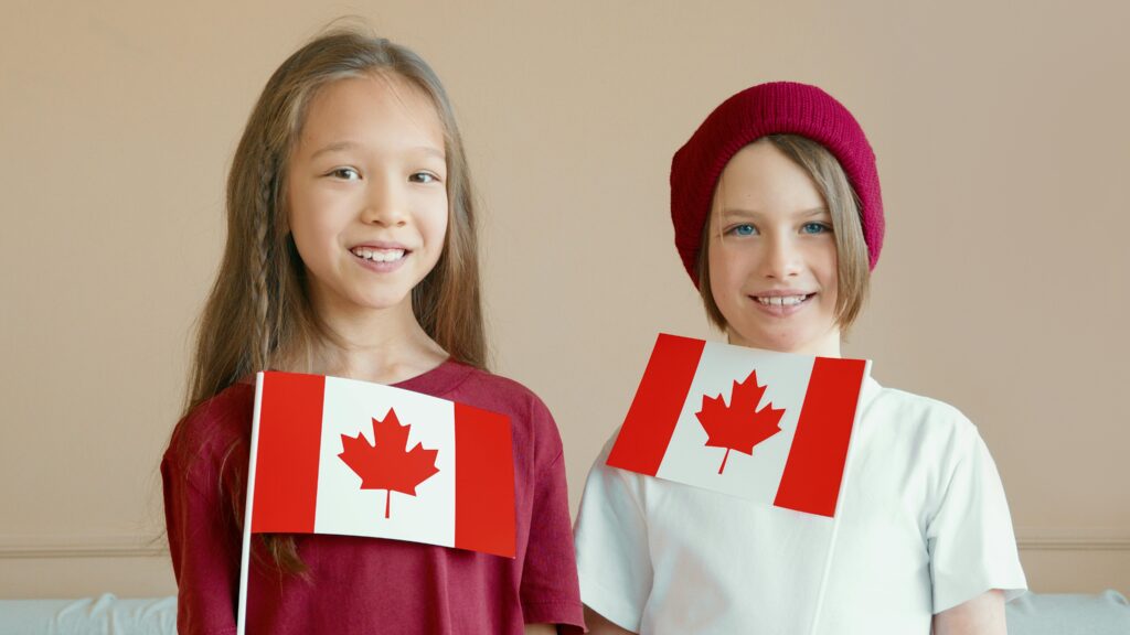 Two smiling children holding Canadian flags indoors, celebrating national pride.