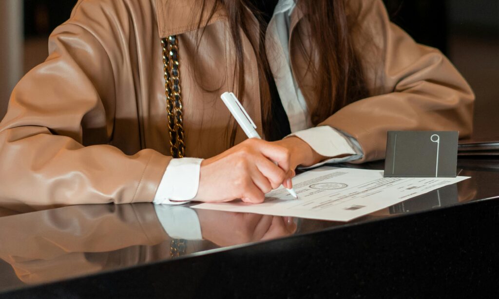 pexels photo 7820383 7820383 Close-up of a woman signing a document at a sleek reception counter, indoor setting.
