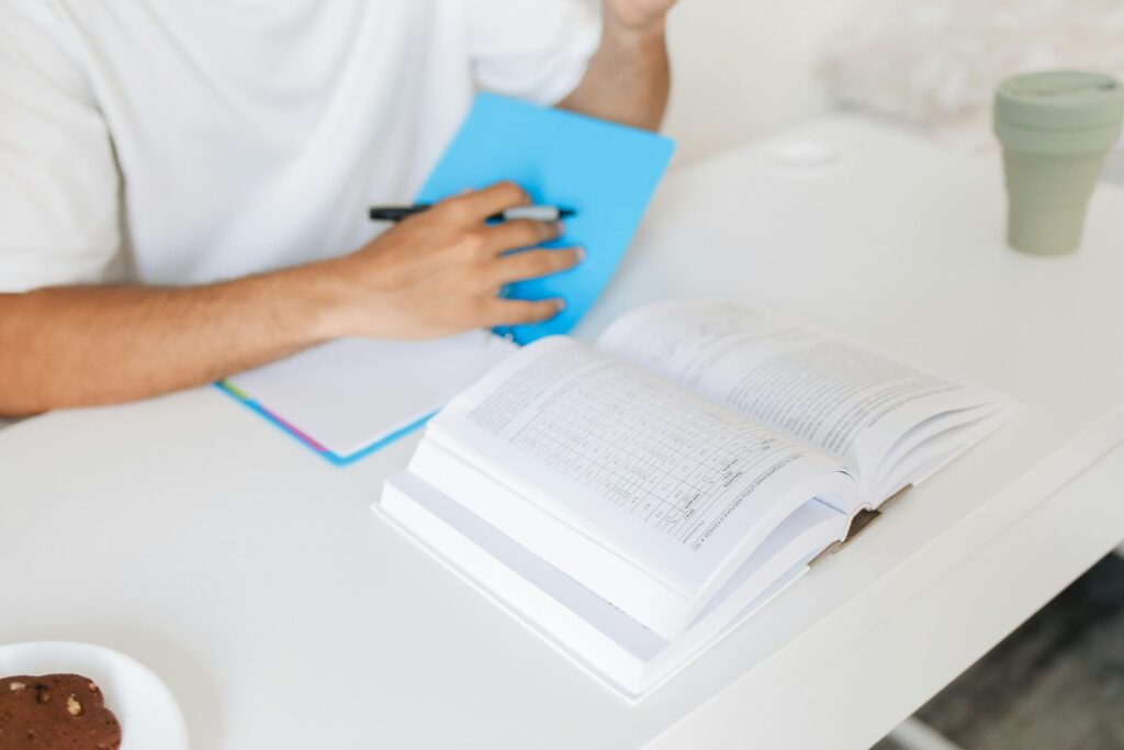 A close-up of an adult studying at a desk with an open book and notebook, capturing a moment of learning.